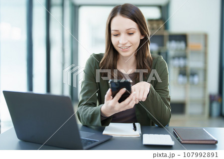 Portrait of a young Asian man showing a smiling face as she uses his phone, computer and financial documents on her desk in the early morning hours. Portrait of a young Asian man showing a smiling face as she uses his phone, computer and financial documents on her desk in the early morning hours. 107992891