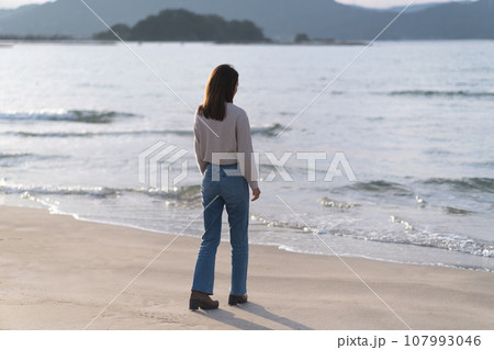 秋の海の砂浜を歩くフレアジーンズをはいた女性（福井県 若狭和田ビーチ） 107993046