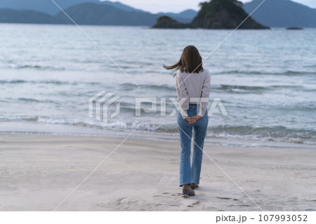 秋の海の砂浜を歩くフレアジーンズをはいた女性（福井県 若狭和田ビーチ） 107993052