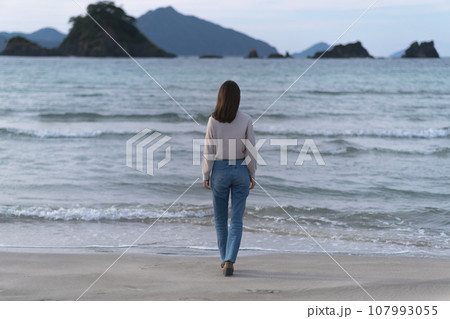 秋の海の砂浜を歩くフレアジーンズをはいた女性（福井県 若狭和田ビーチ） 107993055