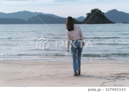 秋の海の砂浜を歩くフレアジーンズをはいた女性（福井県 若狭和田ビーチ） 107993143