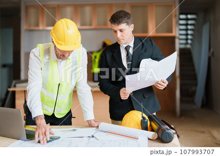 multi ethnic engineer brainstorming and measuring for cost estimating on blueprint and floor plan drawings about design architectural and engineering for houses and buildings. 107993707