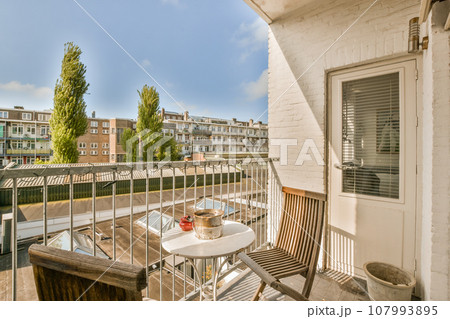a balcony with an outside table and chairs on the left side, there is a blue sky in the background 107993895