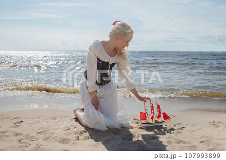 Portrait of perfect young blonde woman with red sail boat on sea beach Portrait of perfect young blonde woman with red sail boat on sea beach 107993899
