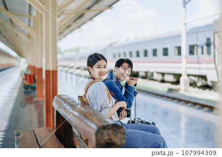 Young couple traveling using a camera to capture memories while waiting for the train at the station.travel concepts Young couple traveling using a camera to capture memories while waiting for the train at the station.travel concepts 107994309