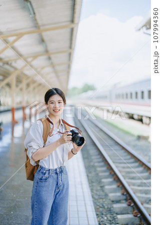 Asian teenage girl traveling using a camera take a photo to capture memories while waiting for a train at the station Asian teenage girl traveling using a camera take a photo to capture memories while waiting for a train at the station 107994360