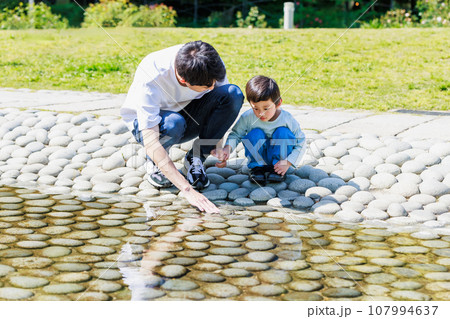 小川でお父さんと水遊びをする子供 107994637