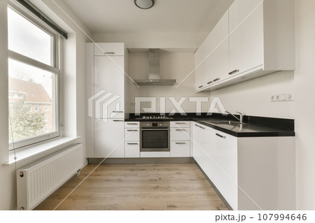 a kitchen with white cupboards and black counter tops on the floor in front of the window looking out onto the street 107994646