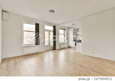 an empty living room with hardwood flooring and white walls, large windows in the room is light wood floors an empty living room with hardwood flooring and white walls, large windows in the room is light wood floors 107994652