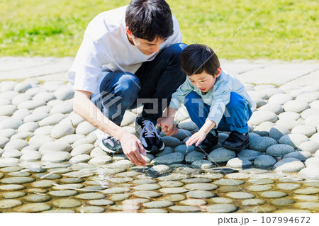 小川でお父さんと水遊びをする子供 107994672