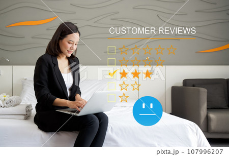 Focused businesswoman perusing through customer reviews on her laptop while sitting comfortably on a bed in a calm and serene environment. Customer review satisfaction feedback survey concept. 107996207