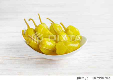 Pickled yellow greek pepper, pepperoncini or friggitelli in bowl on white wooden background Pickled yellow greek pepper, pepperoncini or friggitelli in bowl on white wooden background 107996762