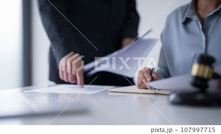 Businessman pointing on document and explaining finance data of business to lawyer while female attorney giving advice consultation about legal agreement and terms of business contract in law firm Businessman pointing on document and explaining finance data of business to lawyer while female attorney giving advice consultation about legal agreement and terms of business contract in law firm 107997715