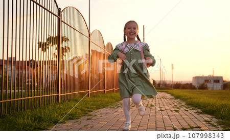 happy child with school backpack runs along way school, children education, child smile laughter, first-grader kid with bag runs happily through school yard, child smile with teeth, kid laughter 107998343