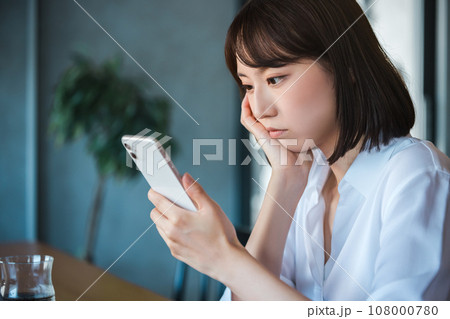 スマートフォンを見て考える若いビジネスウーマン スマートフォンを見て考える若いビジネスウーマン 108000780