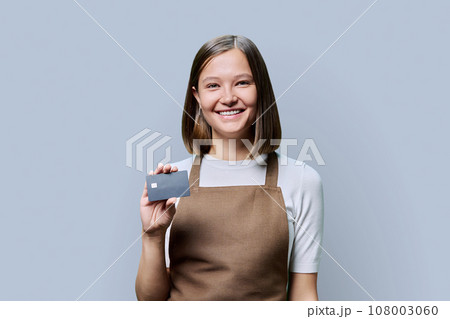 Young happy woman service worker in apron with credit card in hand, on gray background Young happy woman service worker in apron with credit card in hand, on gray background 108003060