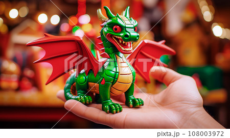 Hand holding a green dragon toy on the background of Christmas decorations. Hand holding a green dragon toy on the background of Christmas decorations. 108003972
