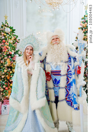 a Father Frost and Snow Maiden in blue costume in the room with christmas trees  108004463