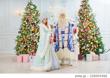 a Father Frost and Snow Maiden in blue costume in the room with christmas trees  108004466
