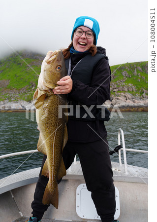 Happy young woman holding big arctic cod. Norway happy fishing. Fisherwoman with cod fish in hands 108004511