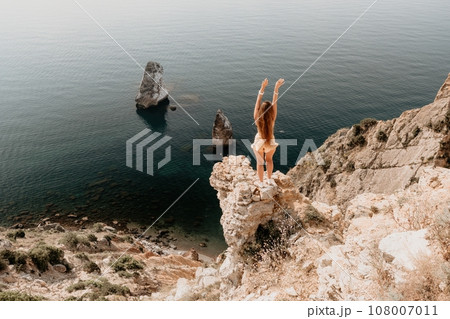 Woman travel sea. Happy tourist enjoy taking picture outdoors for memories. Woman traveler looks at the edge of the cliff on the sea bay of mountains, sharing travel adventure journey 108007011