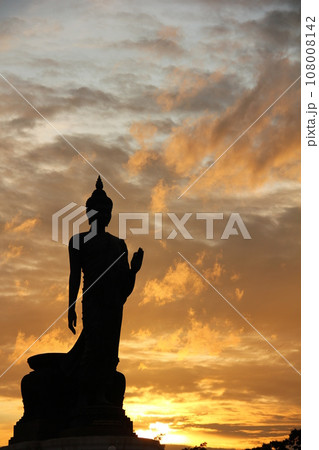 Stand big tall walk Buddha Statue in sun set Light background in park of thailand temple.Yellow orange light silhouette dark shadow of Buddha statue image Lord Buddha. 108008142
