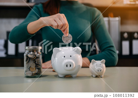 Women are putting coins in a piggy bank for a business that grows for profit and saving money for the future. planning for retirement concept. 108011392