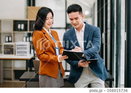 Asian business colleague business presents and explains and using laptop and tablet. Teamwork, financial marketing team, while sitting in office room. Asian business colleague business presents and explains and using laptop and tablet. Teamwork, financial marketing team, while sitting in office room. 108015736