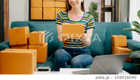 Startup small business SME, Entrepreneur owner woman using smartphone or tablet taking receive and checking online purchase shopping order to preparing pack product box. Startup small business SME, Entrepreneur owner woman using smartphone or tablet taking receive and checking online purchase shopping order to preparing pack product box. 108016080