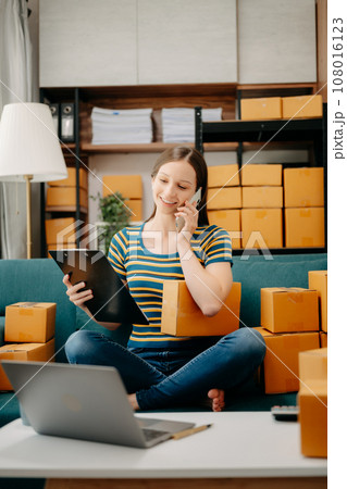 Young business owner woman prepare parcel box and standing check online orders for deliver to customer on tablet, laptop Shopping Online concept. on sofa .. 108016123