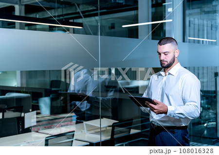 Handsome businessman with digital tablet computer looking in device screen working in modern office. Handsome businessman with digital tablet computer looking in device screen working in modern office. 108016328