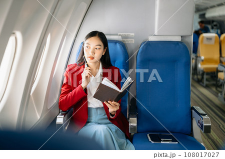 Young Asian executive excels in first class, multitasking with digital tablet, laptop and smartphone. Travel in style, work with grace.. 108017027