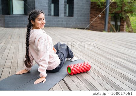 Young Indian woman practicing yoga pilates in the park, sitting on fitness mat 108017061