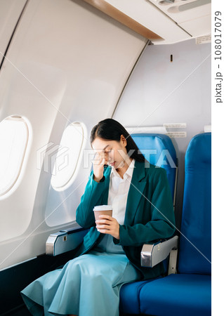 Photo of a frustrated woman sitting on an airplane with her head in her hands. Asian woman sitting in a seat. 108017079