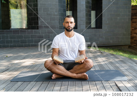 Portrait of handsome man holding sadhu boards while sitting in yoga lotus pose 108017232