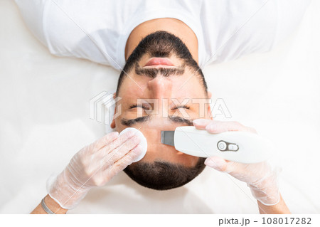 Ultrasonic facial cleansing for young handsome man in professional beauty clinic. View above. Ultrasonic facial cleansing for young handsome man in professional beauty clinic. View above. 108017282
