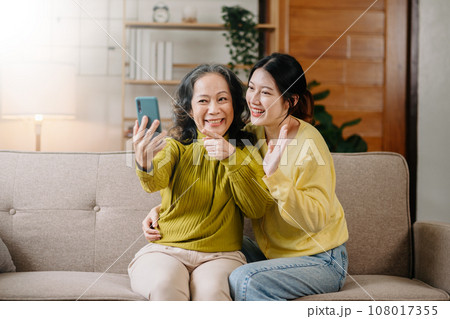 Happy adult granddaughter and senior grandmother having fun enjoying talk sit on sofa in living room at home. Happy adult granddaughter and senior grandmother having fun enjoying talk sit on sofa in living room at home. 108017355