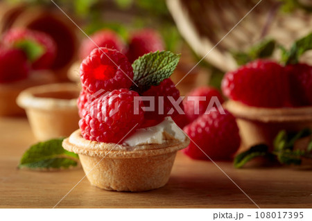 Tartlets with fresh raspberries and mint on a wooden table. 108017395