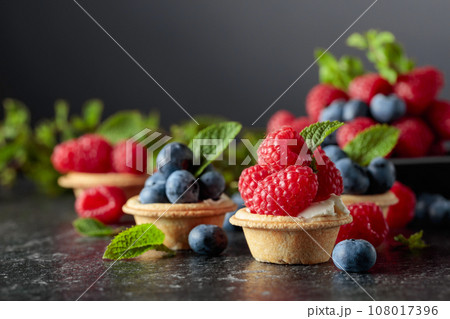Small tartlets with fresh raspberries and blueberries on a black background. Small tartlets with fresh raspberries and blueberries on a black background. 108017396