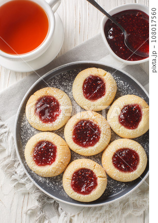 Thumbprint cookies are classic sugar cookies with a jam-filled center closeup on the plate on the white wooden table. Vertical top view Thumbprint cookies are classic sugar cookies with a jam-filled center closeup on the plate on the white wooden table. Vertical top view 108017560