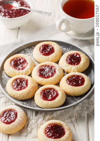 Thumbprint a buttery and crumbly vanilla cookie dough filled with delicious and tart raspberry jam closeup on the plate served with tea. Vertical 108017567