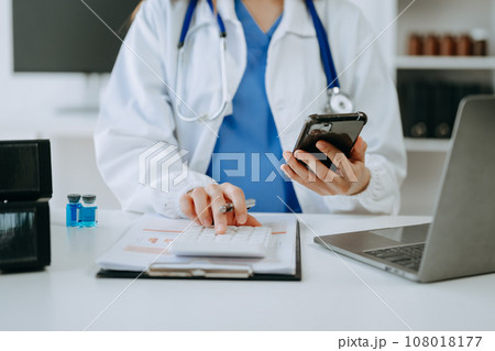 Healthcare costs and fees concept.Hand of smart doctor used a calculator and smartphone, tablet for medical costs at hospital Healthcare costs and fees concept.Hand of smart doctor used a calculator and smartphone, tablet for medical costs at hospital 108018177