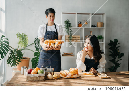 A man in the kitchen preparing a meal with Bread and fruit in cozy kitchen while his wife hugging him. sweet home. A man in the kitchen preparing a meal with Bread and fruit in cozy kitchen while his wife hugging him. sweet home. 108018925