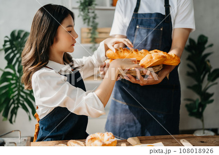 A man in the kitchen preparing a meal with Bread and fruit in cozy kitchen while his wife hugging him. sweet home. A man in the kitchen preparing a meal with Bread and fruit in cozy kitchen while his wife hugging him. sweet home. 108018926