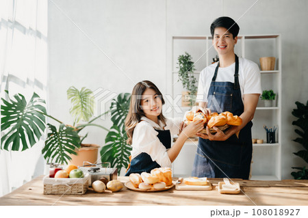 A man in the kitchen preparing a meal with Bread and fruit in cozy kitchen while his wife hugging him. sweet home. A man in the kitchen preparing a meal with Bread and fruit in cozy kitchen while his wife hugging him. sweet home. 108018927