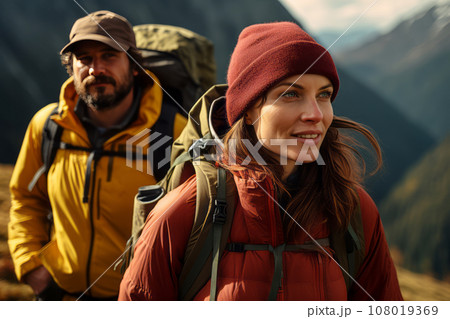 Happy young couple of tourists against the backdrop of stunning mountain landscape. Cheerful hikers in modern bright outfits with backpacks walking along mountain path. Active sports and travel. 108019369