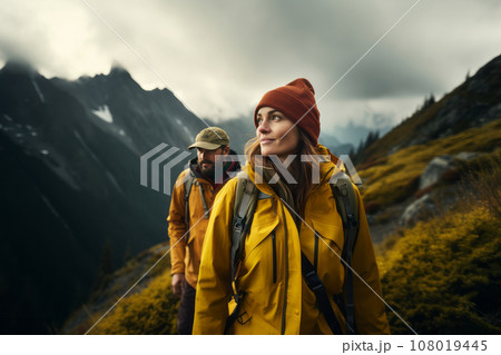 Happy young couple of tourists against the backdrop of stunning mountain landscape. Cheerful hikers in modern bright outfits with backpacks walking along mountain path. Active sports and travel. 108019445