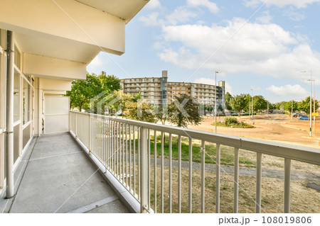 a balcony with white railings and trees in the foregrounded area on the other side of the building 108019806