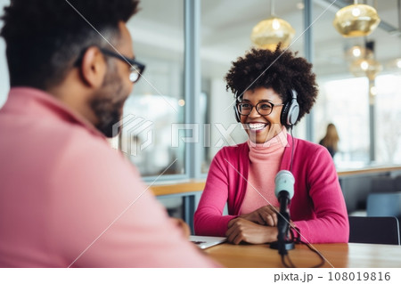 Beautiful multiethnic blogger couple hosting a podcast in a studio. Smiling woman and man wearing headphones sitting at a table with microphones and chatting cheerfully. Modern media technologies. Beautiful multiethnic blogger couple hosting a podcast in a studio. Smiling woman and man wearing headphones sitting at a table with microphones and chatting cheerfully. Modern media technologies. 108019816