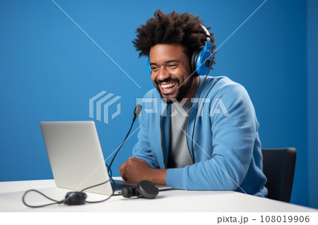 Happy smiling African American blogger hosting podcast in studio. Influencer uses laptop, headphones and microphone to record live stream for the subscribers. Vlogger shooting video for the channel. Happy smiling African American blogger hosting podcast in studio. Influencer uses laptop, headphones and microphone to record live stream for the subscribers. Vlogger shooting video for the channel. 108019906